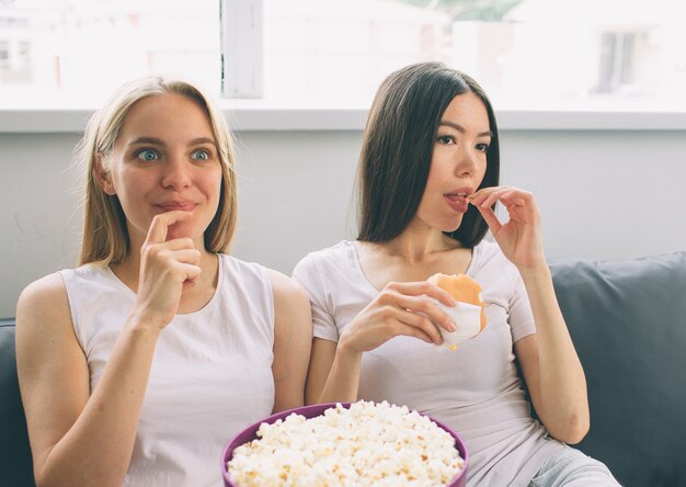 Le donne mangiano popcorn e hamburger e guardano la tv