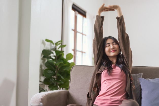 Le donne sedute sul divano alzano le braccia per allungarsi e respirare al mattino con lo stile di vita a casa