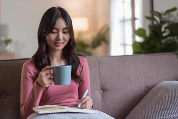 Le donne si divertono sul divano a bere tè e scrivere appunti sul diario nello stile di vita di casa