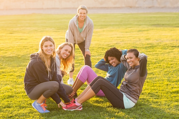 Le donne sportive sorridenti che fanno siedono durante la classe di forma fisica