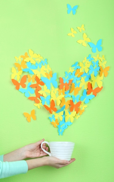 Le farfalle di carta volano fuori dalla tazza sul fondo verde della parete