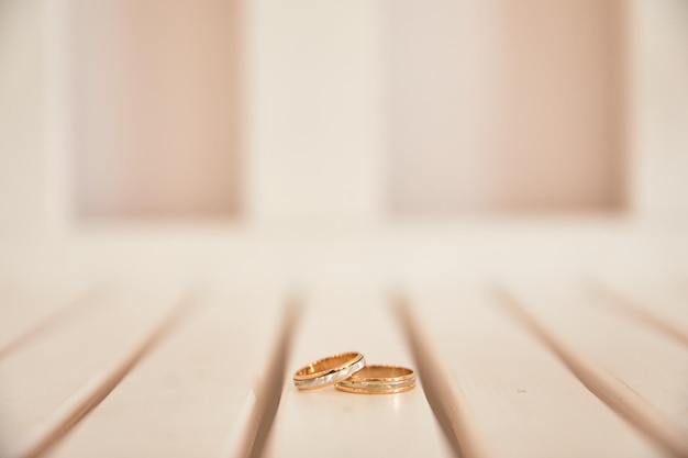 Le fedi nuziali dorate giacciono su assi di legno bianco anelli su uno sfondo di legno chiaro
