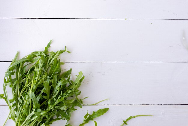 Le foglie di insalata di rucola fresca sono distese su un tavolo di legno. Posiziona sotto il testo