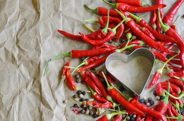 Le forme di cuore di alluminio hanno riempito di piccoli peperoncini su carta d'annata. Concetto di caldo amore e passione