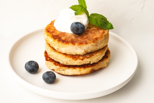 Le frittelle di ricotta o le frittelle di ricotta impilano con panna acida, foglia di menta e mirtillo di farina di mandorle e cocco senza glutine nella vista ravvicinata del piatto bianco. Concetto di colazione. Messa a fuoco morbida selettiva.