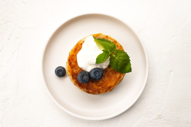 Le frittelle di ricotta o le frittelle di ricotta impilano con panna acida, menta, mirtillo di mandorle e farina di cocco senza glutine nel piatto bianco vicino vista dall'alto. Mangiare sano prima colazione. Messa a fuoco morbida selettiva