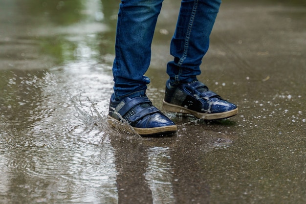 Le gambe del bambino in primo piano delle scarpe da tennis, il bambino salta in pozzanghere. Salute, concetto di infanzia felice.