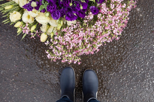 Le gambe dell'uomo con uno stivale di gomma blu in piedi vicino a un cesto con bellissimi fiori da giardino dopo la pioggia