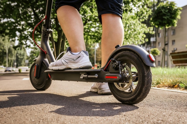 Le gambe dell'uomo in scarpe da ginnastica bianche cavalcano su uno scooter elettrico nero sull'asfalto