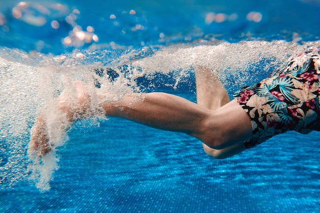 Le gambe dell'uomo nuotano sott'acqua in piscina in estate