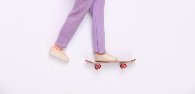 Le gambe della bambola cavalcano su skateboard su sfondo bianco Minimalismo