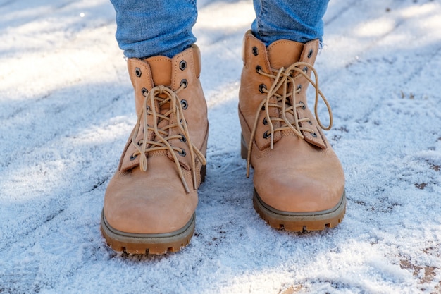 Le gambe della donna agli stivali marroni che stanno sulla neve