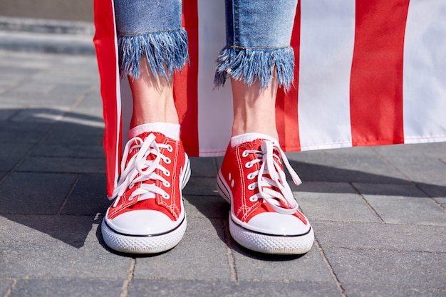 Le gambe della donna in jeans eleganti e scarpe da tennis rosse Bandiera americana sullo sfondo