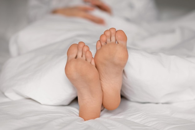 Le gambe della donna millenaria caucasica stanca giace sul letto sotto la coperta bianca dormono di notte goditi il riposo rilassati