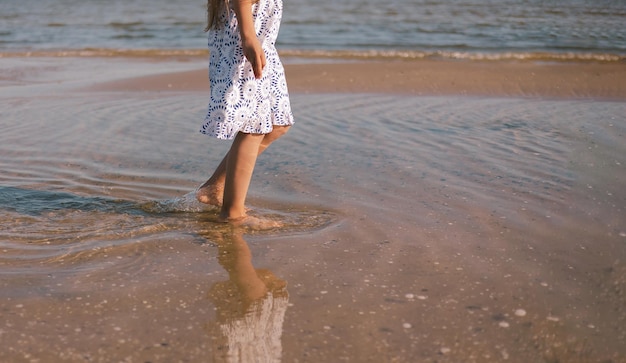 Le gambe della ragazza si chiudono a piedi nudi sulla sabbia e sulla riva del mare