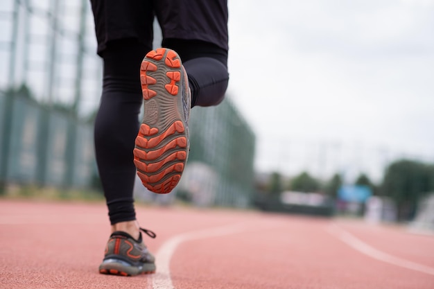 Le gambe di un corridore con delle comode scarpe da ginnastica corrono lungo una pista gommata in uno stadio urbano