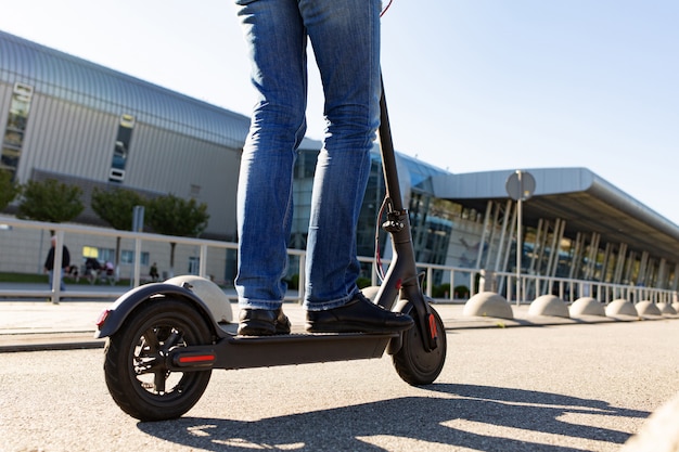 Le gambe di un uomo in piedi su uno scooter elettrico parcheggiato sul marciapiede