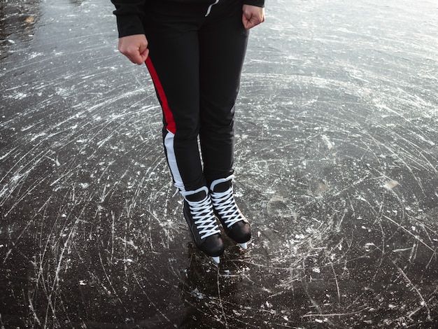 Le gambe di una ragazza in hockey nero pattina sul ghiaccio di un primo piano del lago. Sullo sfondo una foresta