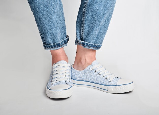 Le gambe femminili in jeans corti e scarpe da tennis stanno su un bianco