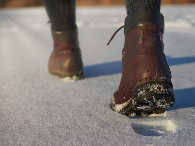 Le gambe femminili in stivali impermeabili in pelle marrone stanno facendo un'escursione invernale sulla neve fresca. Moda casual, calzature alla moda.