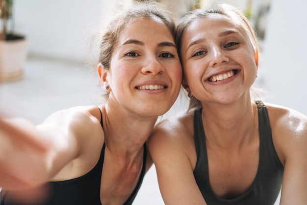 Le giovani amiche in forma praticano lo yoga prendendo selfie sul telefono cellulare nello studio di yoga