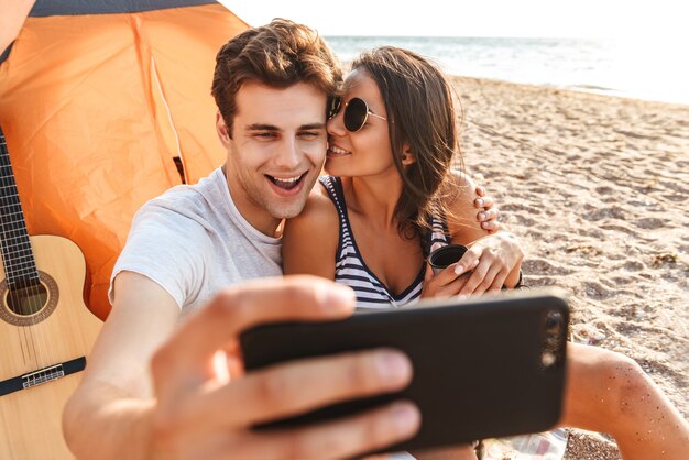 Le giovani coppie amorose sveglie allegre fanno selfie dal telefono cellulare sulla spiaggia all'aperto