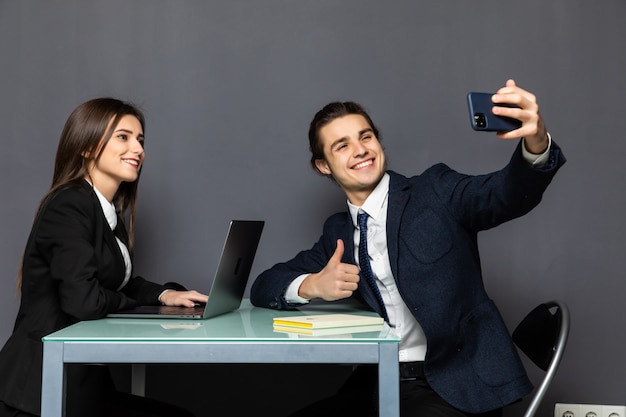 Le giovani coppie dei colleghi di affari prendono il selfie dai telefoni cellulari che si siedono sulla tavola