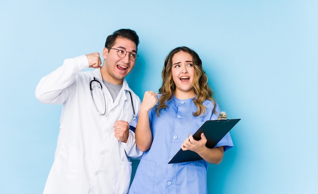 Le giovani coppie di medico che posano in una parete blu hanno isolato il pugno d'innalzamento dopo una vittoria, concetto del vincitore.