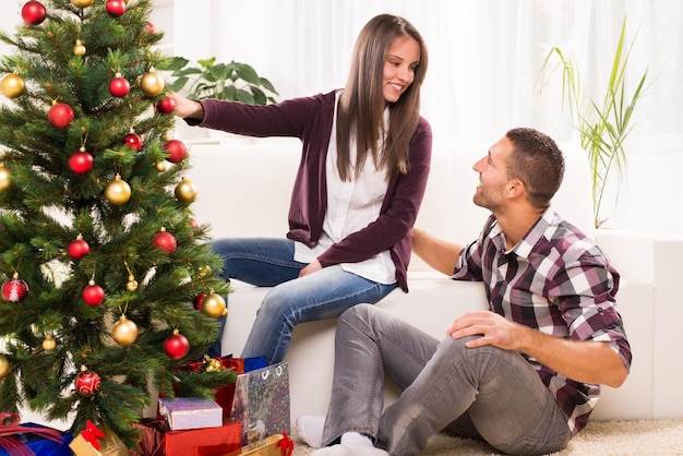 Le giovani coppie felici si divertono a decorare l'albero di Natale a casa.