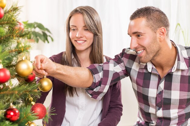 Le giovani coppie felici si divertono a decorare l'albero di Natale a casa.