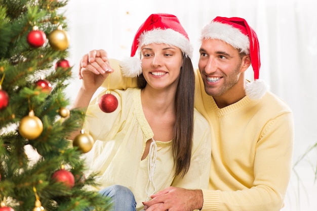 Le giovani coppie felici si divertono a decorare l'albero di Natale a casa.