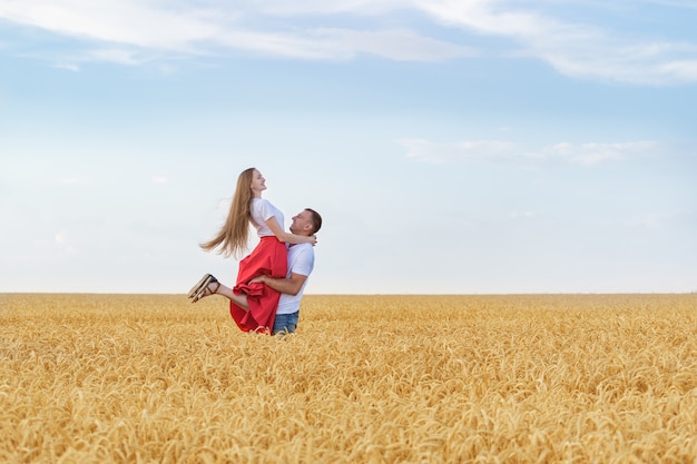 Le giovani coppie felici si divertono in campagna. L'uomo tiene la donna sulle mani in mezzo al campo di grano