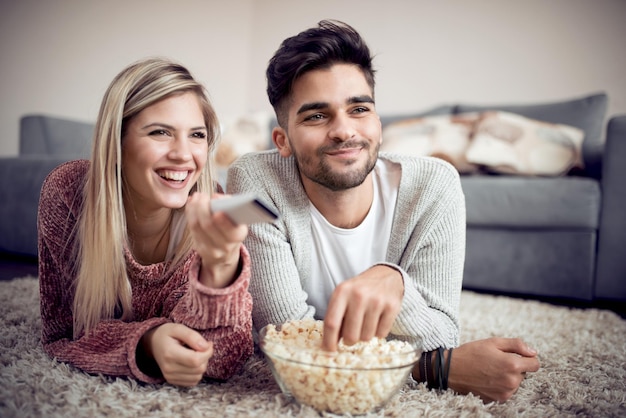 Le giovani coppie guardano la TV sul pavimento della casa