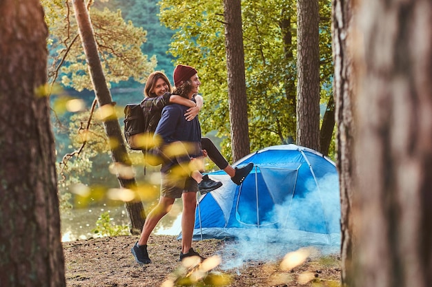 Le giovani coppie romantiche si divertono nella foresta estiva vicino alla loro tenda. L'uomo tiene la donna, lei lo abbraccia.