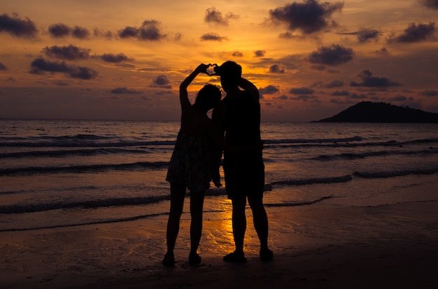 Le giovani coppie stanno sulla spiaggia con il tramonto