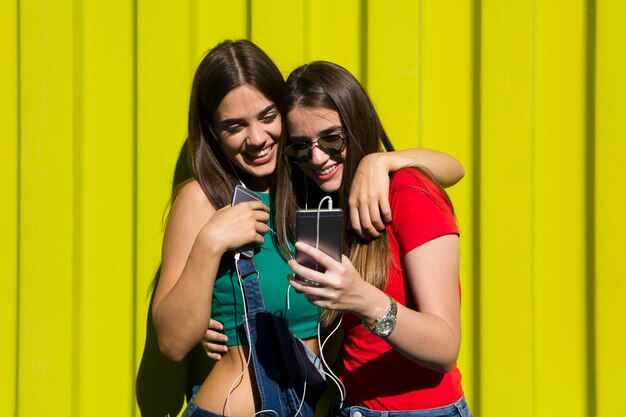 Le giovani donne all'aperto contro la parete verde ascoltano musica in cuffia e si divertono