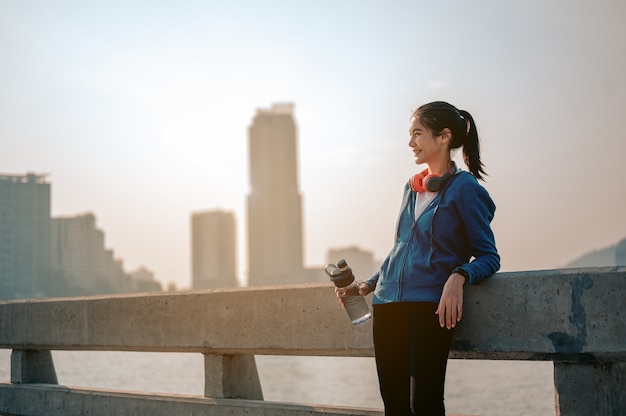 Le giovani donne asiatiche bevono acqua e si riposano dopo aver fatto jogging un allenamento mattutino in città