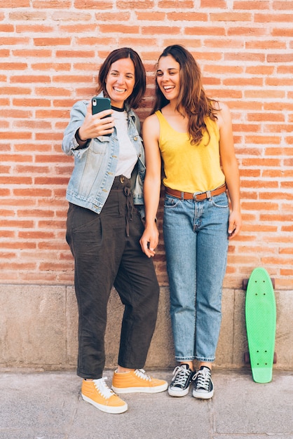 Le giovani donne coppia facendo un selfie in un muro di mattoni.