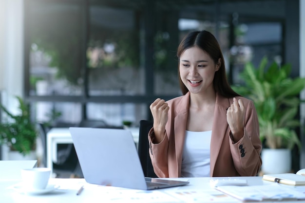 Le giovani donne d'affari asiatiche mostrano gioiosa espressione di successo sul lavoro sorridendo felicemente con un computer portatile in un ufficio moderno