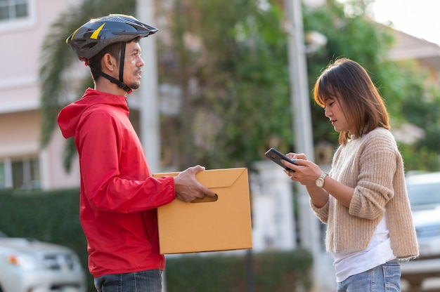 Le giovani donne firmano per ritirare la merce tramite il telefono intelligente, concetto di servizio di corriere