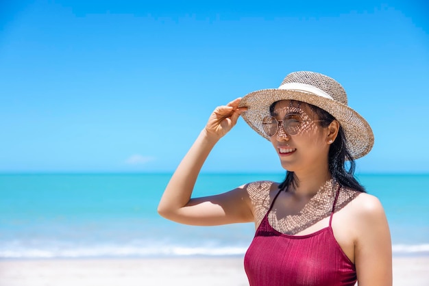 Le giovani donne in bikini e cappello di paglia stanno sulla spiaggia tropicale godendo della vista dell'oceano della spiaggia