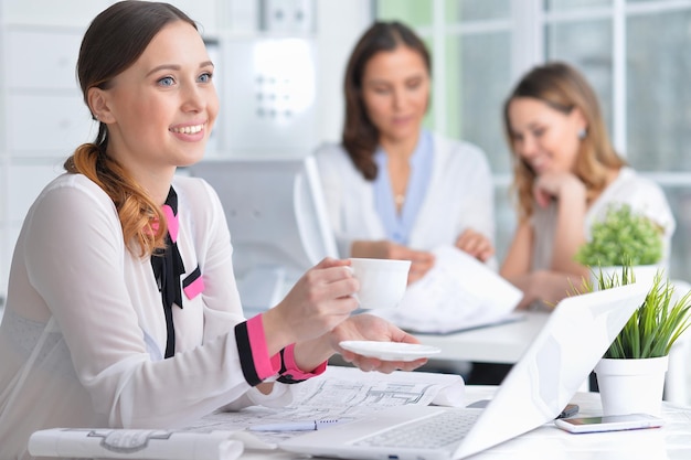 Le giovani donne si siedono al tavolo e lavorano in un ufficio moderno con un laptop