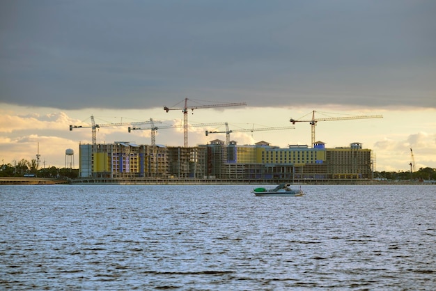 Le gru a torre e la struttura a telaio di edifici residenziali alti sul cantiere di costruzione sulla costa della baia marittima Sviluppo immobiliare sul lungomare