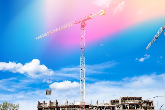 Le gru edili lavorano sul sito di creazione sullo sfondo del cielo blu. Vista dal basso della gru industriale. Concetto di costruzione di condomini e ristrutturazione di alloggi. Copia spazio