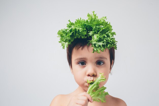 Le insalate della tenuta del bambino si chiudono su. Divertente cappello con insalata