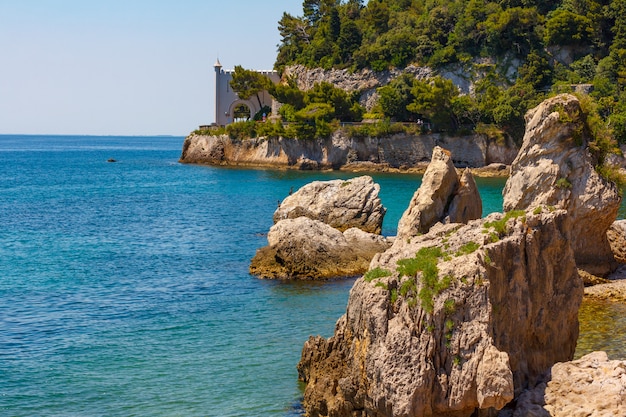 Le isole rocciose si trovano nell'acqua blu del mare Adriatico. Grandi pietre sono in mezzo al mare non lontano da montagne verdi e da un castello sospeso sopra l'acqua del mare.