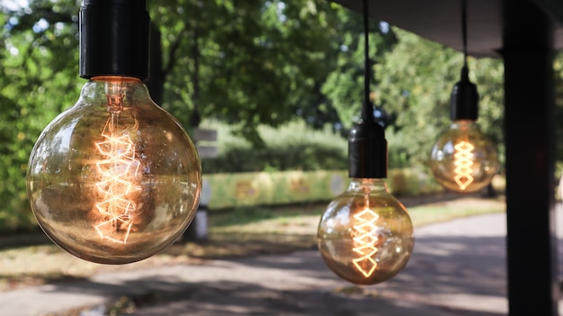 Le lampadine a incandescenza Edison sono appese in stile loft retrò. Primo piano della decorazione della caffetteria. Street decor Lanterne luminose Luce calda. Messa a fuoco morbida, sfondo strada sfocato.