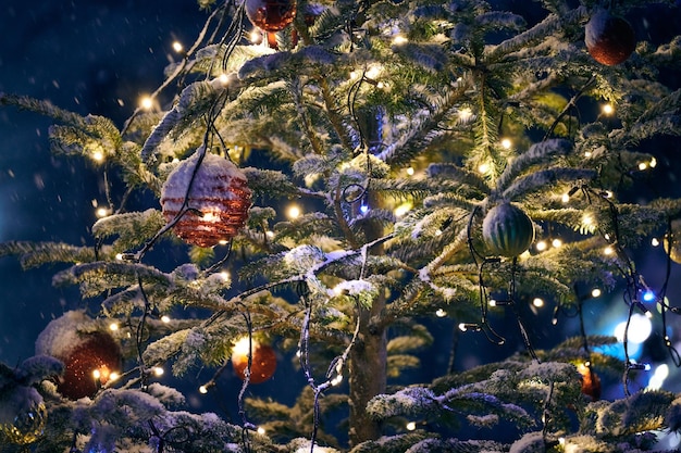 Le lampadine dell'albero di Natale con le ghirlande gialle hanno coperto la neve all'aperto dell'albero di natale con le lampadine rosse decorative