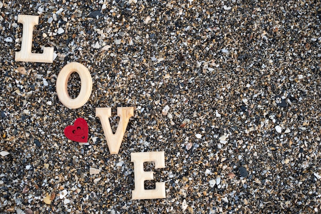 Le lettere di legno che formano la parola amano con un cuore rosso su un fondo della spiaggia sand.concept San Valentino