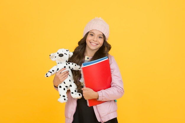 Le lezioni iniziano. felice piccola ragazza tenere cane giocattolo. vacanze invernali e vacanze. felicità dell'infanzia. sviluppo dell'assistenza all'infanzia. libri per la cura dei bambini. vita quotidiana dell'allievo. sfondo giallo studentessa. di nuovo a scuola.